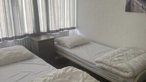 A room with two single beds, a small bedside table, and a window with curtains.