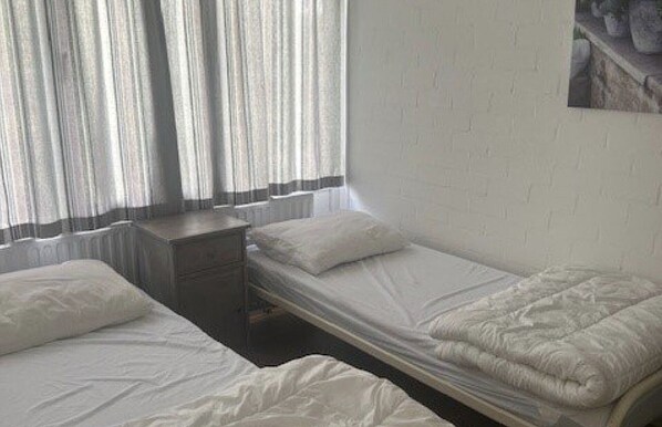 A room with two single beds, a small bedside table, and a window with curtains.