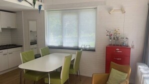 A modern kitchen with a dining area, a red cabinet, and a window with blinds.