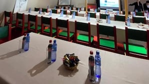 Ein Konferenzraum mit Holzboden, grünen gepolsterten Stühlen, weißen Tischen und Wasserflaschen.
