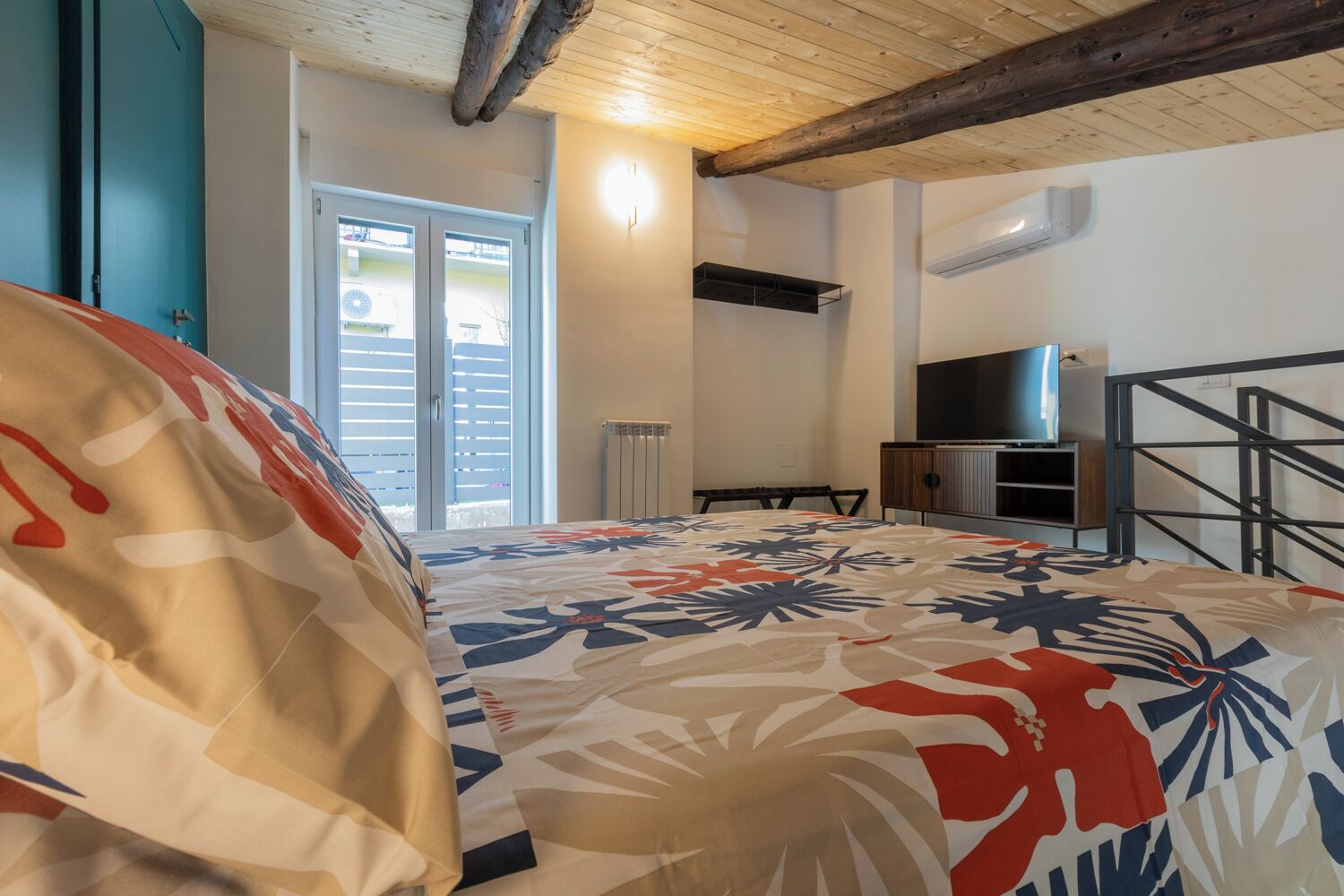 Ein Schlafzimmer mit Bett, Fernseher, Heizkörper und einem Fenster mit Jalousien.