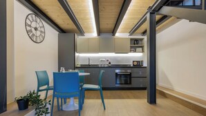 Una cocina moderna con horno empotrado, microondas y lavaplatos. Hay un comedor con sillas azules y una pequeña mesa.