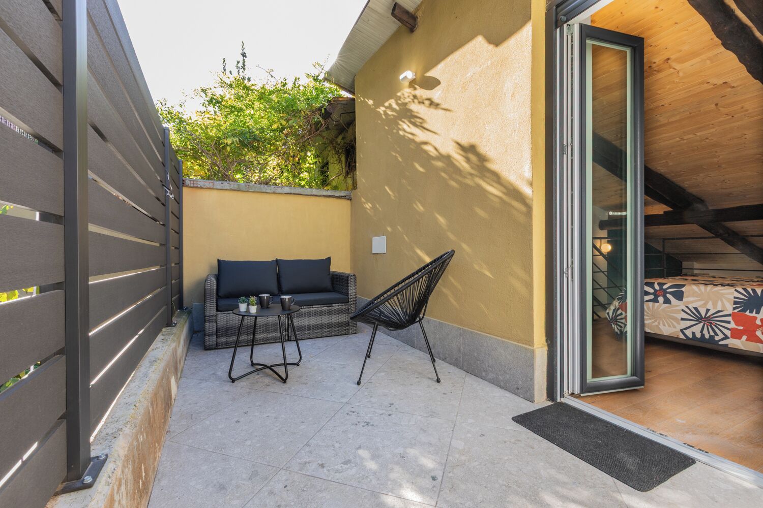 A small outdoor seating area with a sofa and two chairs, a tiled floor, and a wooden ceiling.