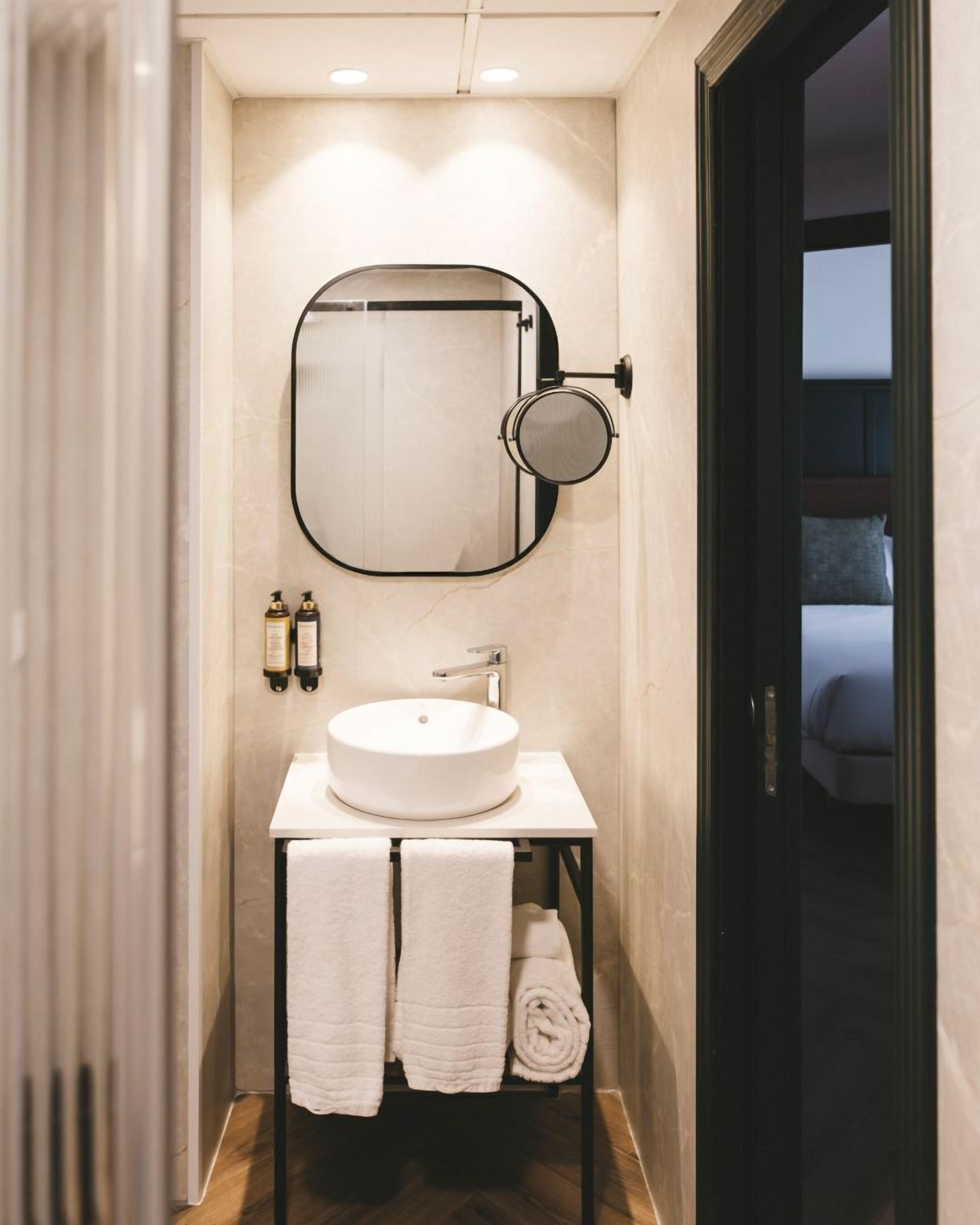 A bathroom with a round sink, a mirror, and two towels.