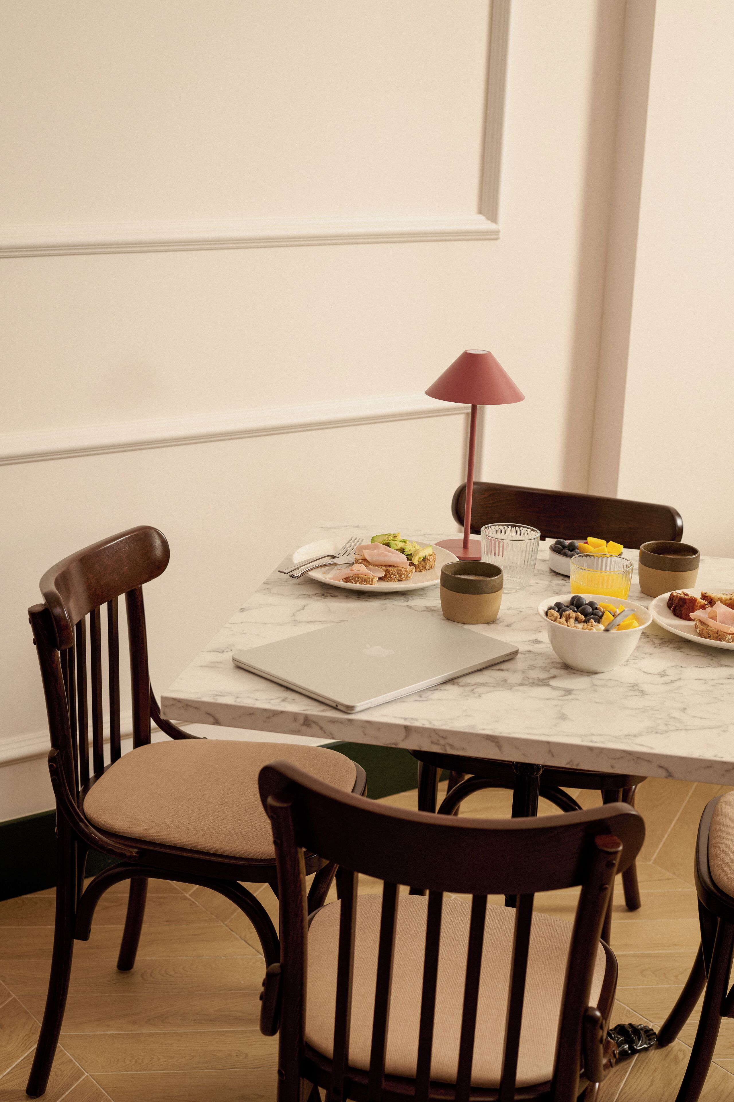 A dining table with a laptop, plates of food, and a lamp.