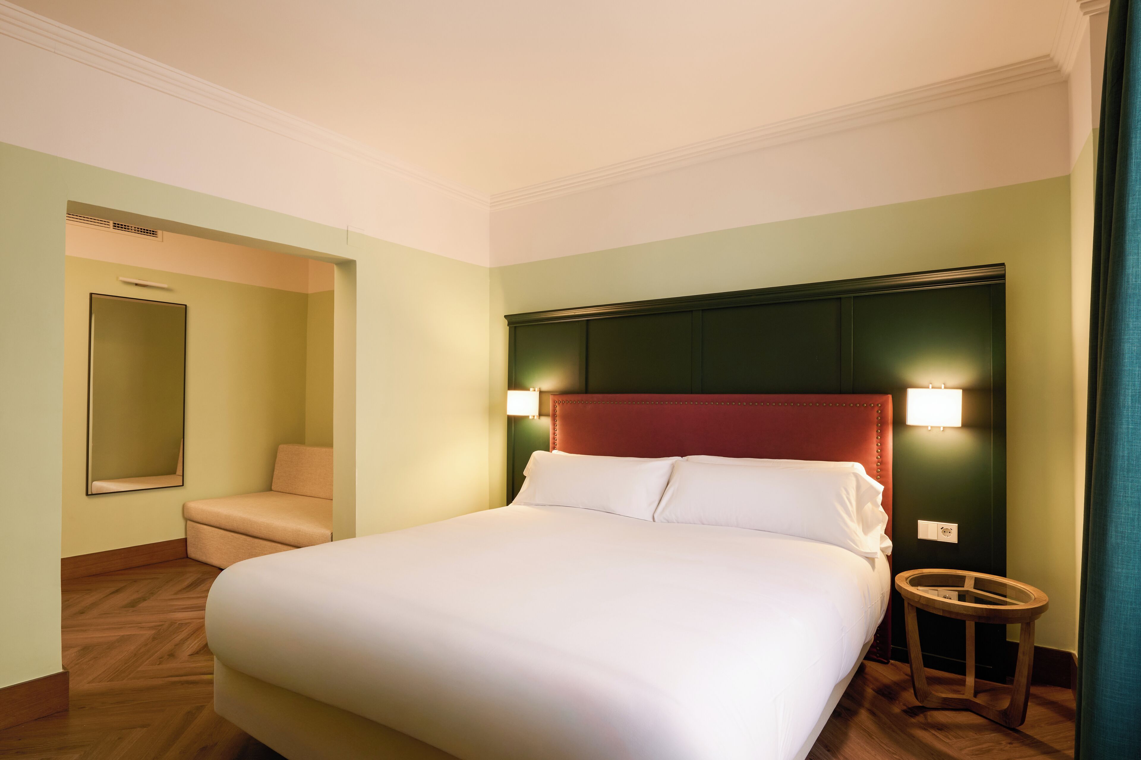 Ein Hotelzimmer mit einem großen Bett, einer kleinen Sitzecke, einem Spiegel und einem Nachttisch.