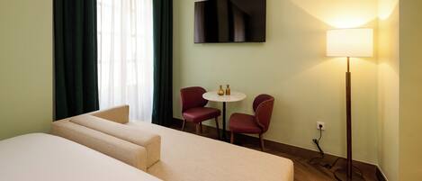 A hotel room with a large bed, a small table with two chairs, a TV mounted on the wall, and a floor lamp.