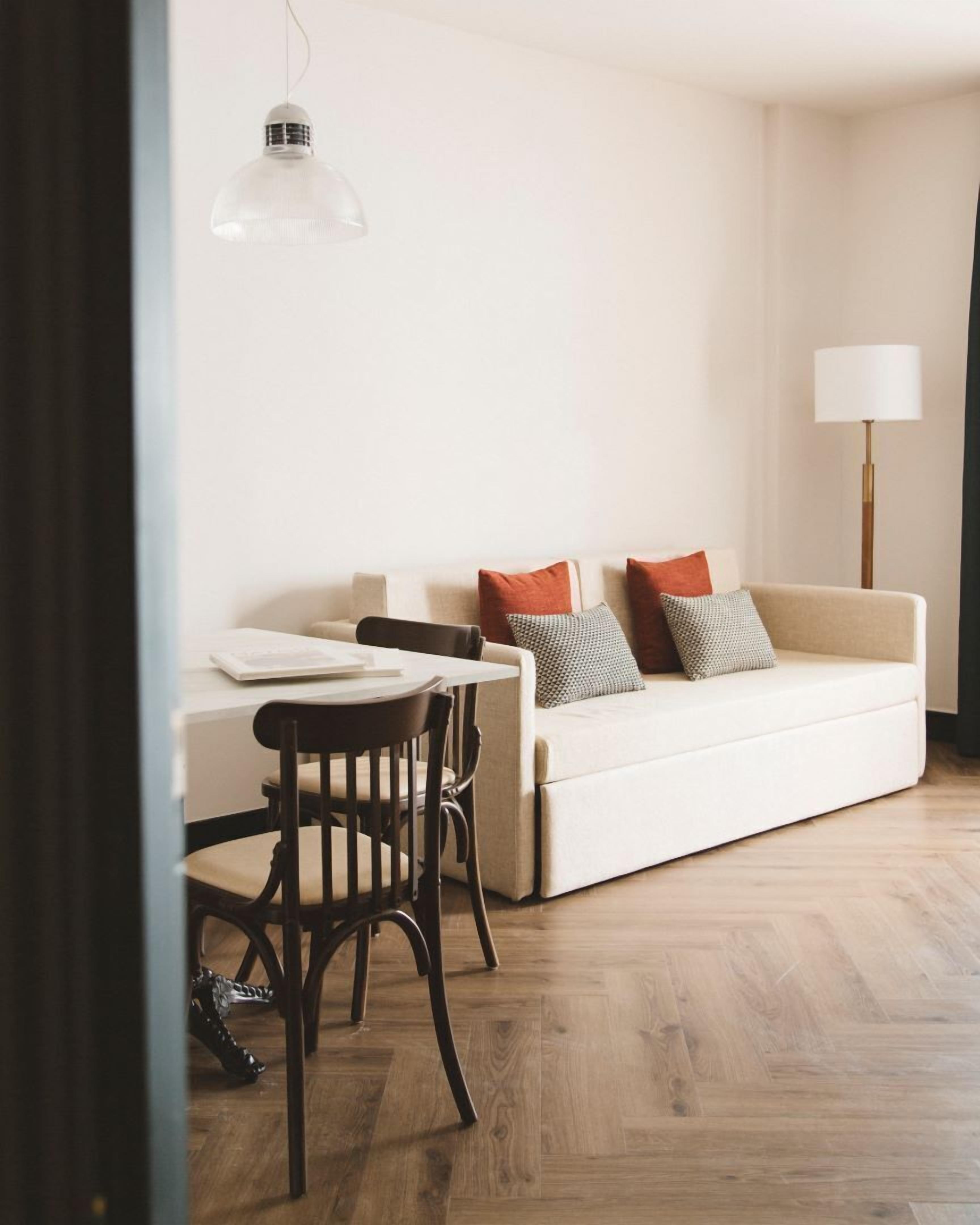 A modern living room with a white sofa, a dining table, and a lamp.
