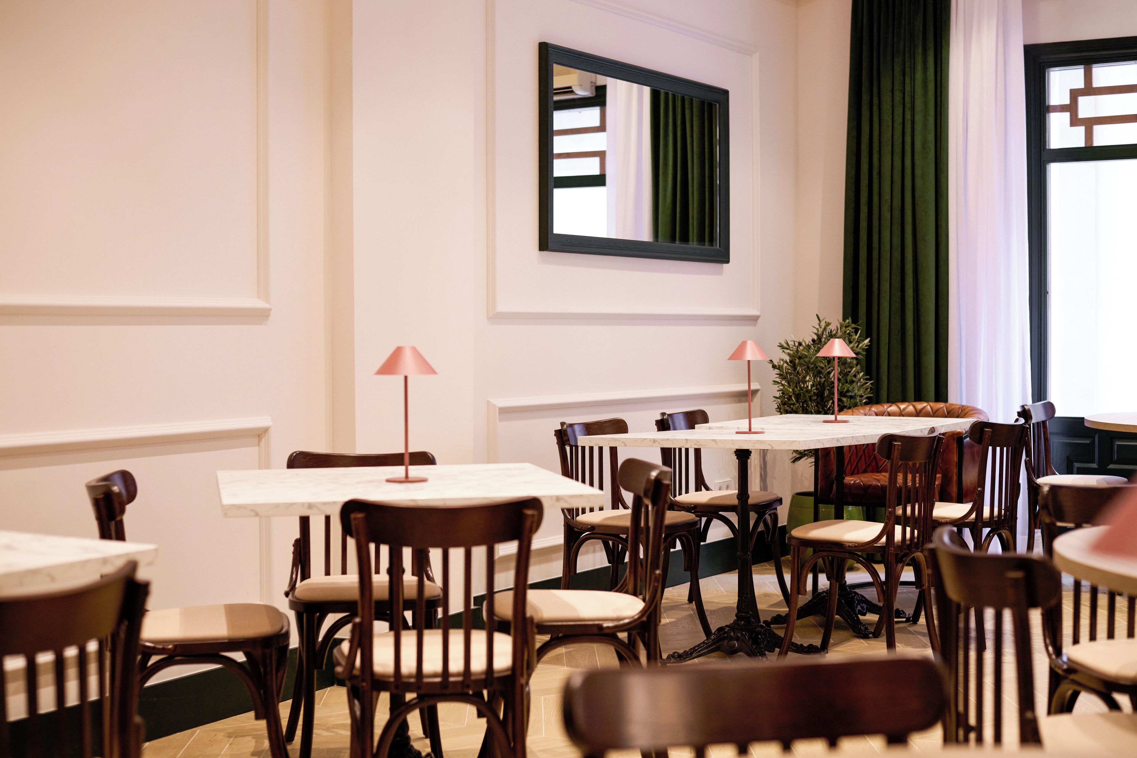 Un espace repas avec plusieurs tables et chaises, un miroir au mur et un rideau vert.
