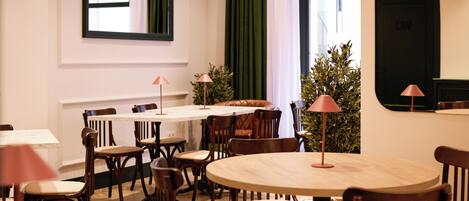 A dining area with round tables and wooden chairs, a green curtain, and a potted plant.