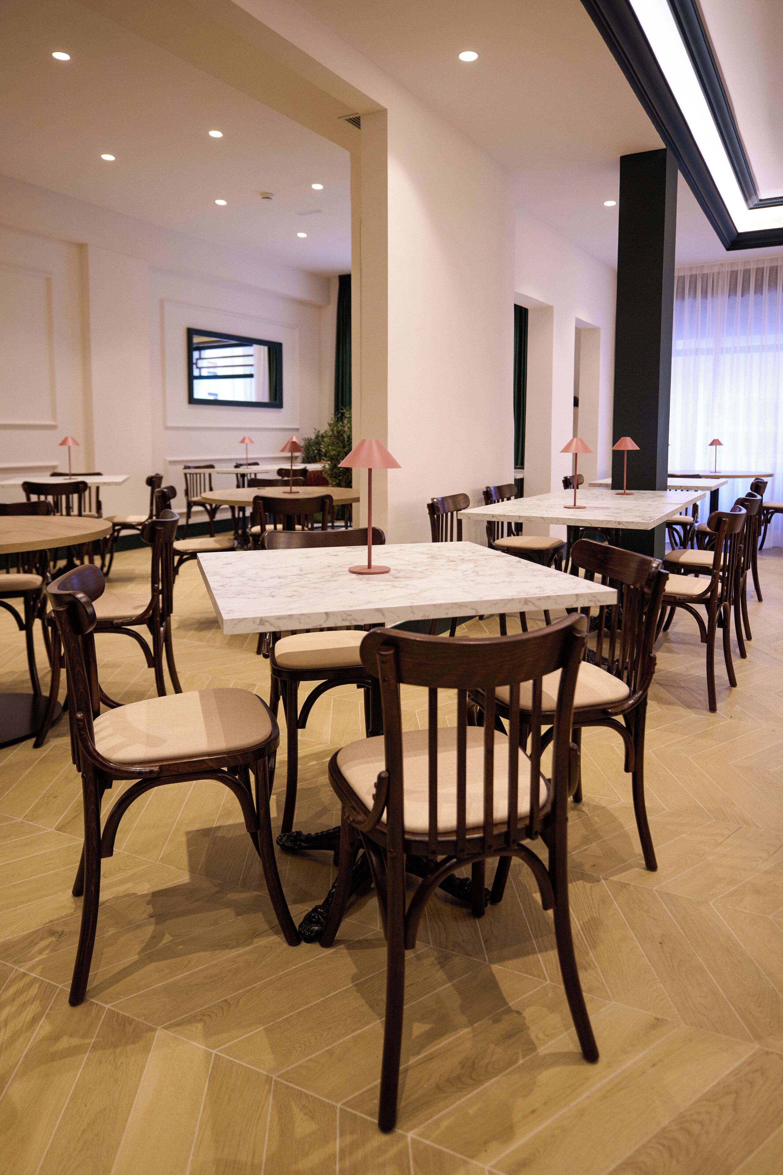 A dining area with multiple tables and chairs, a television mounted on the wall, and a large window with curtains.