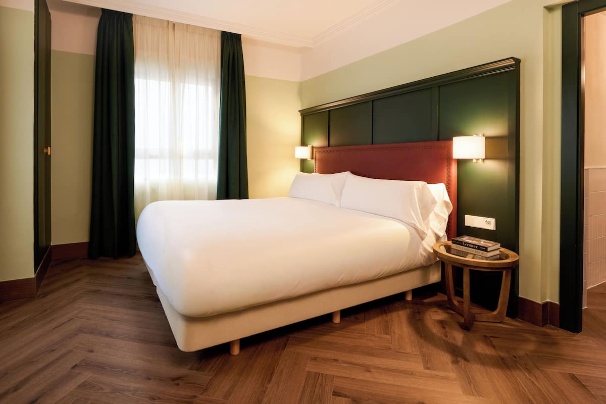 A hotel room with a large bed, wooden flooring, green walls, and a red headboard.