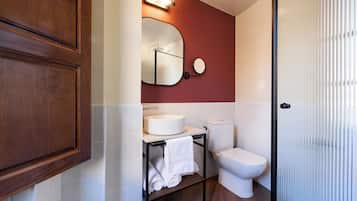 Un baño con un mueble de madera, un espejo redondo, un lavabo blanco, un inodoro y un perchero para toallas.