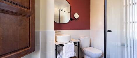 A bathroom with a wooden cabinet, a round mirror, a white sink, a toilet, and a towel rack.