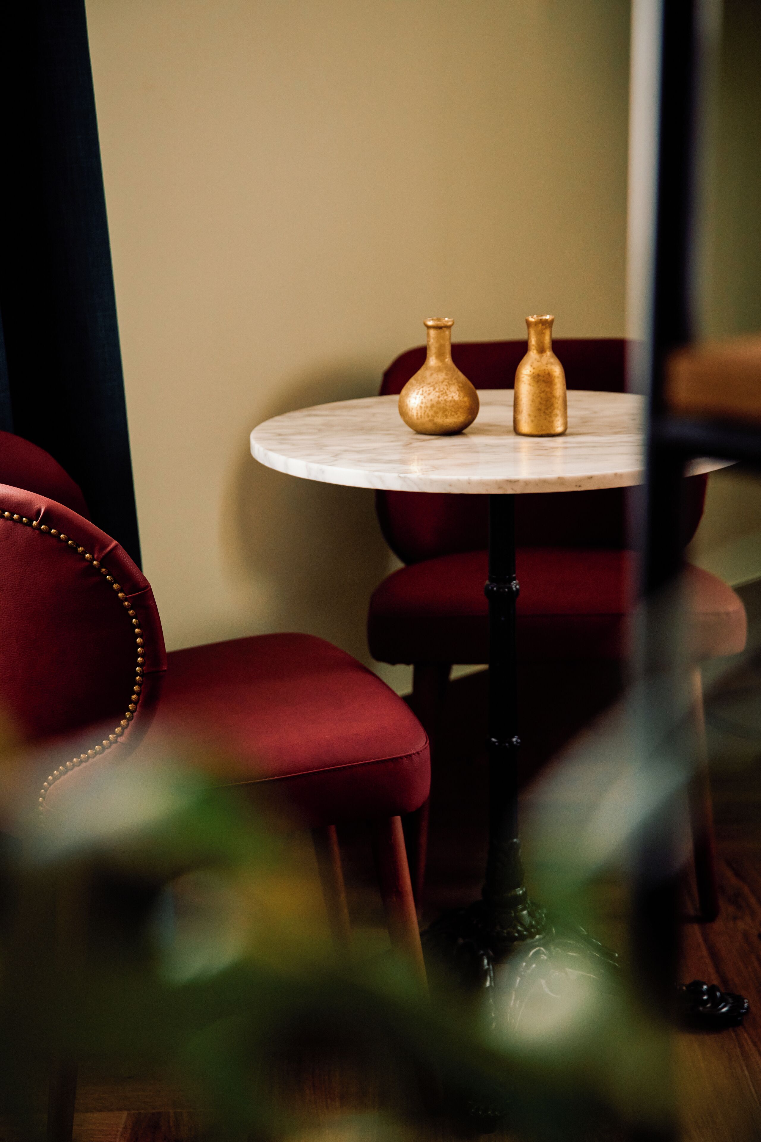 A round table with two golden vases, a red upholstered chair, and a dark wooden floor.