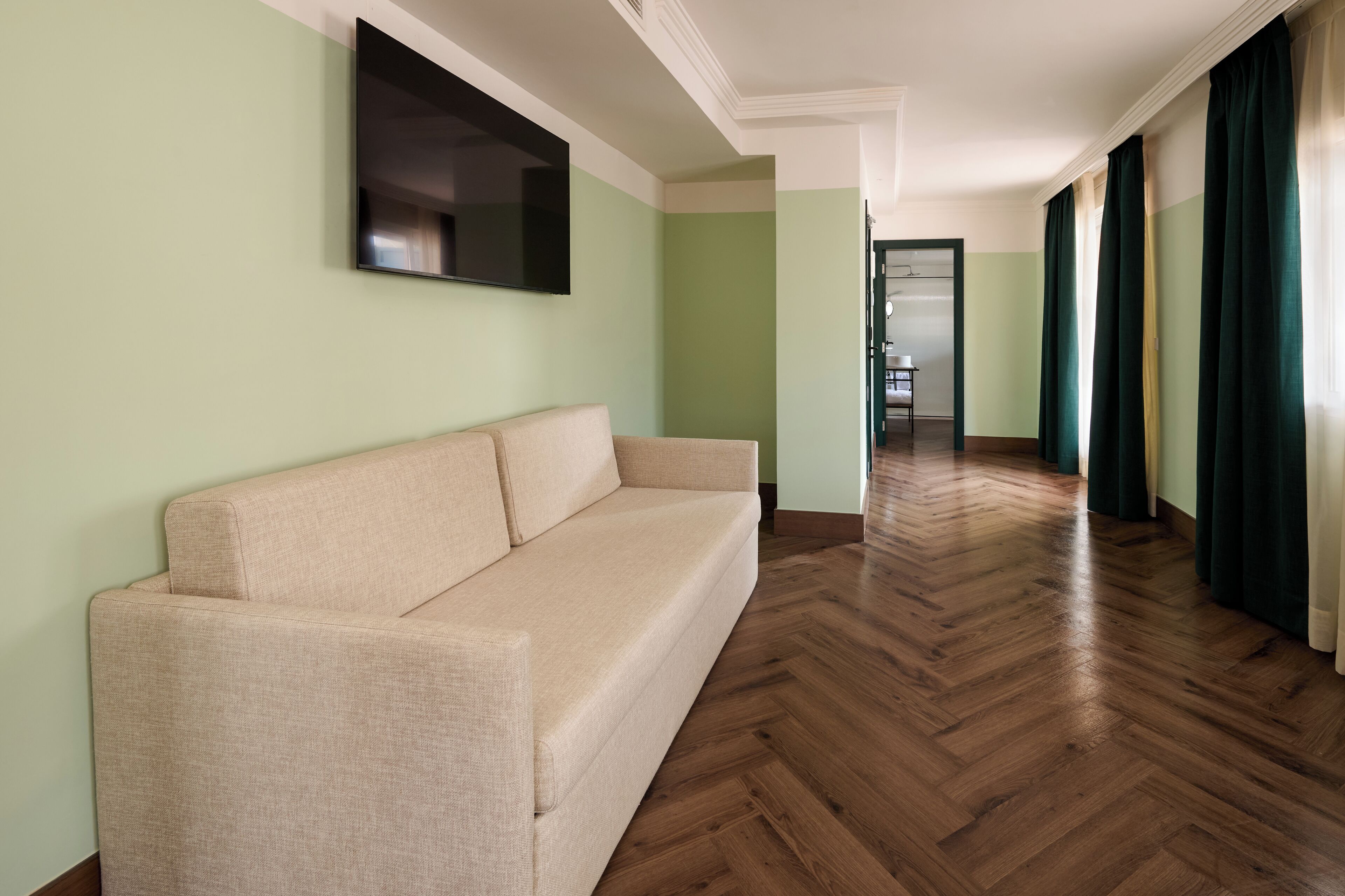 Un pasillo con un sofá color beige, piso de madera y paredes verdes.