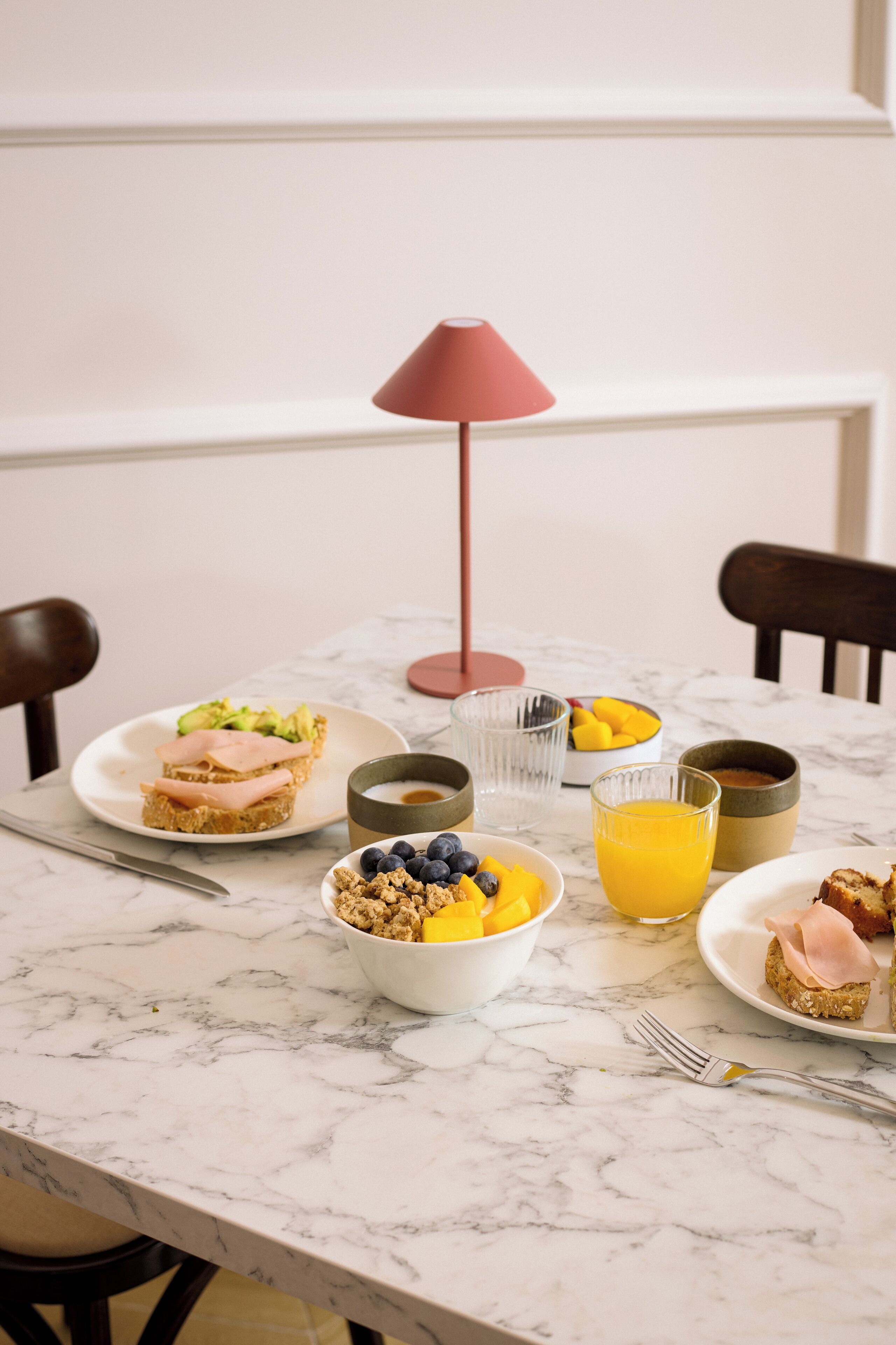 A breakfast table with plates of food, bowls, and a glass of orange juice.