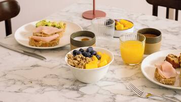 Una mesa de desayuno con platos de comida, tazones y un vaso de jugo de naranja.