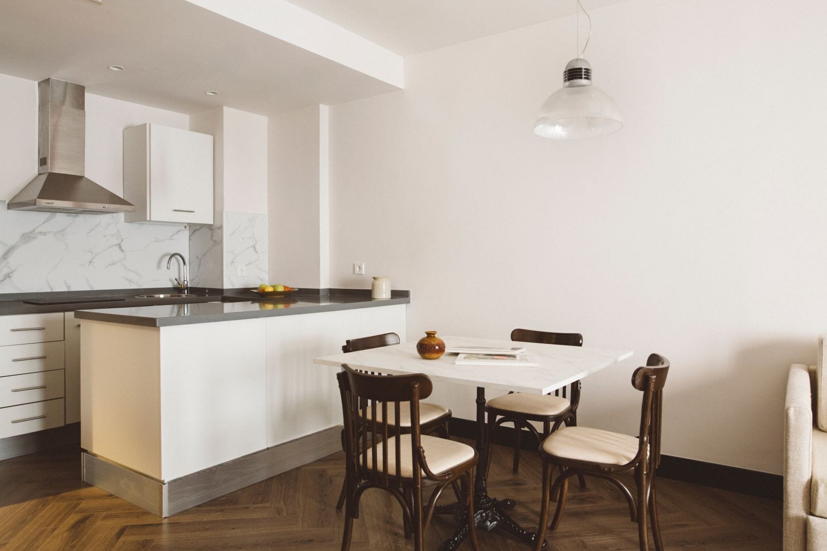 A modern kitchen with a marble countertop, white cabinets, a central island, and a hanging light fixture.