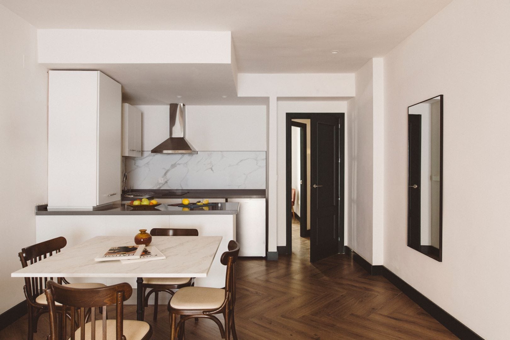 Une cuisine moderne avec des meubles blancs, un plan de travail en marbre et un coin repas comprenant une table blanche et des chaises en bois.