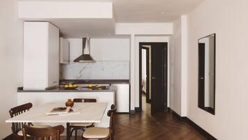 Una cocina moderna con armarios blancos, encimera de mármol y comedor con mesa blanca y sillas de madera.
