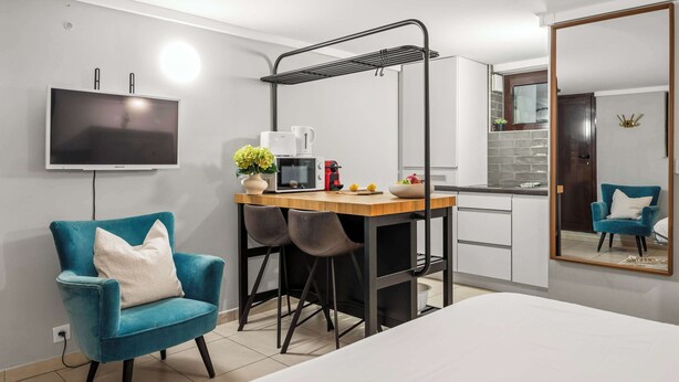 Ett modernt hotellrum med en säng, ett skrivbord med en stol, en TV, en liten köksdel och en spegel.
