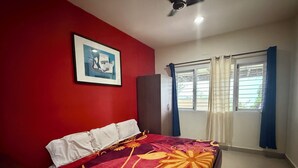 A bedroom with a bed, a wardrobe, a ceiling fan, and a window with curtains. - Nilgiris Inn (Kotagiri)
