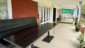 A covered outdoor seating area with a bench, a brick wall, and potted plants. - Nilgiris Inn (Kotagiri)