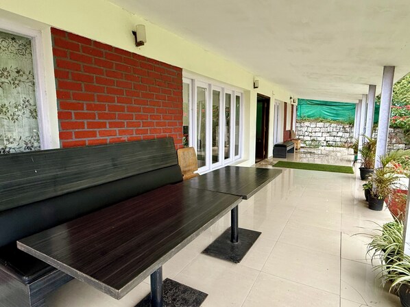 A covered outdoor seating area with a bench, a brick wall, and potted plants. - Nilgiris Inn (Kotagiri)
