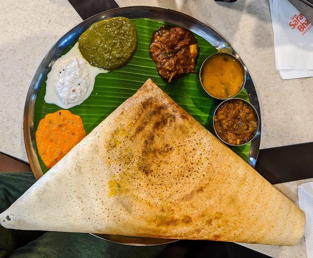 Dosa triangular con diversos chutneys y sambar sobre un plato de hoja de plátano.