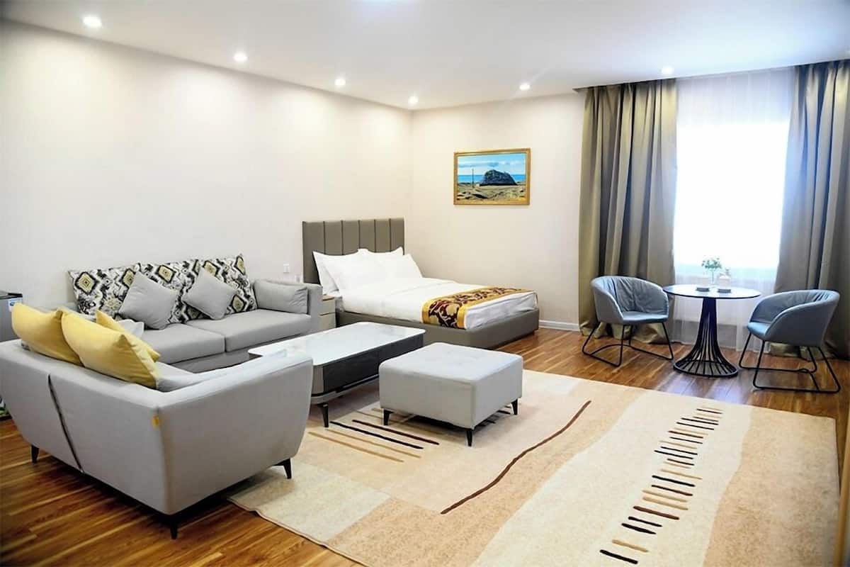A modern hotel room with a sofa, a bed, a coffee table, a small table, and two chairs.
