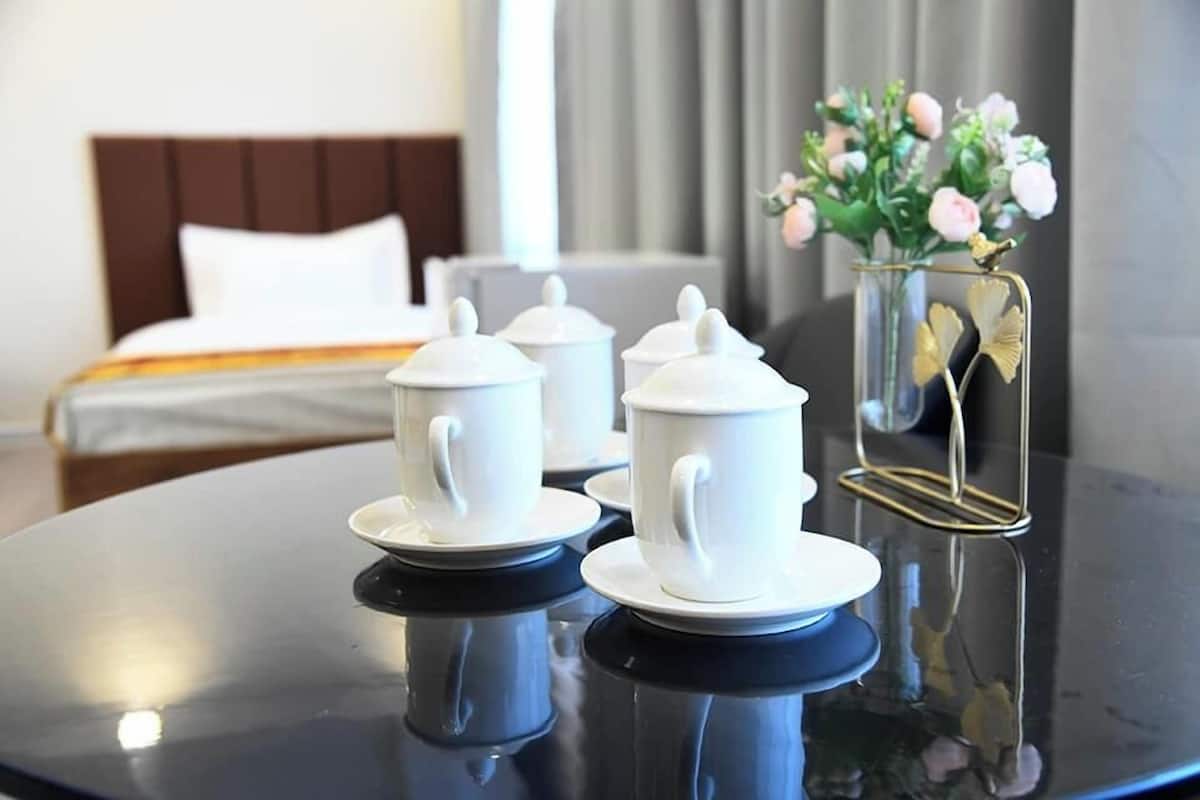 A neatly arranged table with white teapots and cups, a vase with flowers, and a bed in the background.