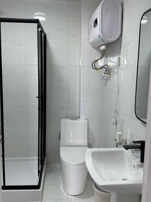 A bathroom with a glass-enclosed shower, a toilet, and a sink with a mirror.