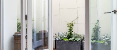 Eine Glastür führt auf eine Terrasse mit Topfpflanzen und einem gefliesten Boden.