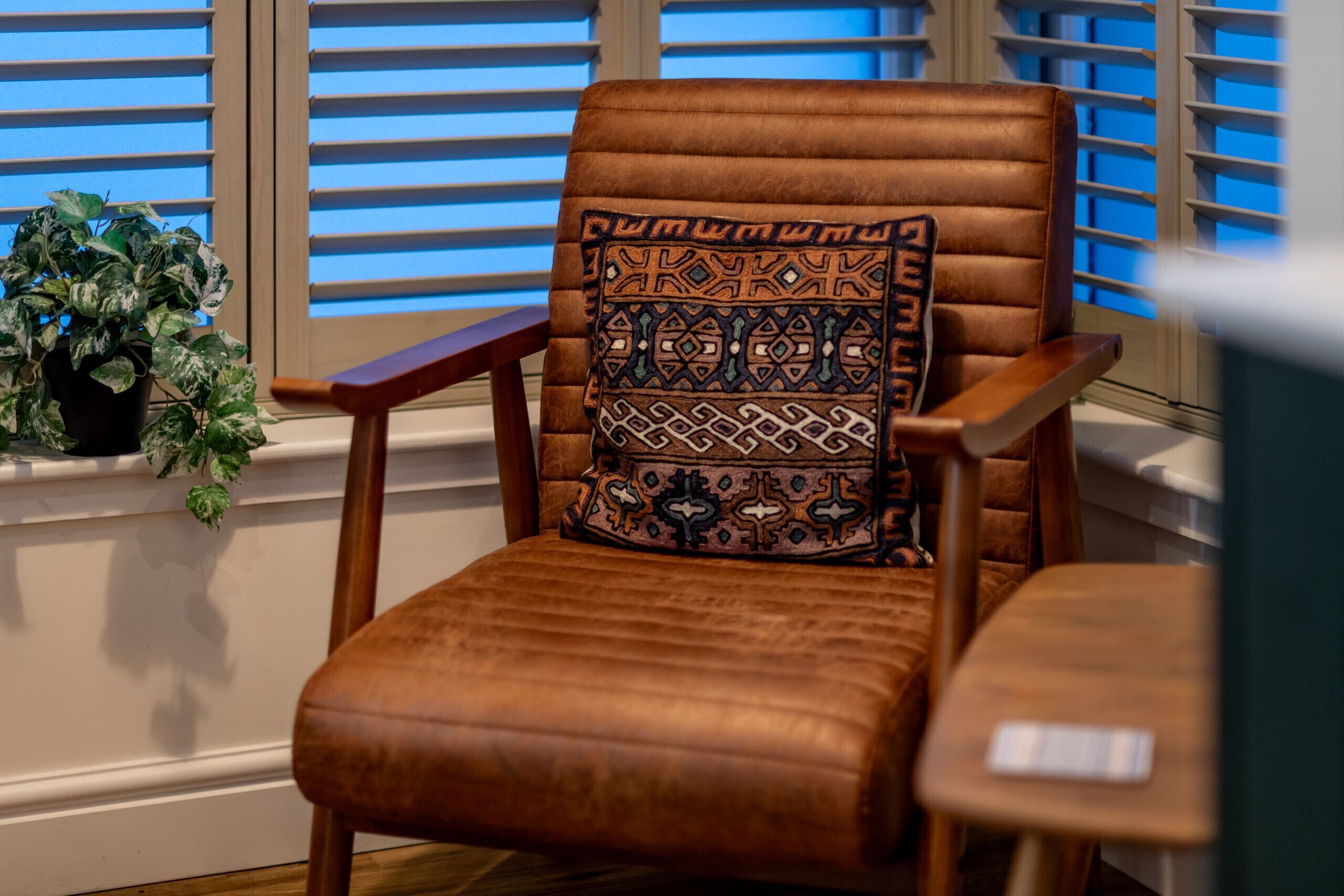 A brown leather armchair with a patterned cushion, positioned by a window with blinds.