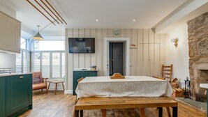A dining area with a wooden table and bench, a television mounted on the wall, and a stone fireplace. - Toll Green View | Elie (Elie)