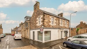 A street view with a stone building, parked cars, and a '20 zone' sign. - Toll Green View | Elie (Elie)