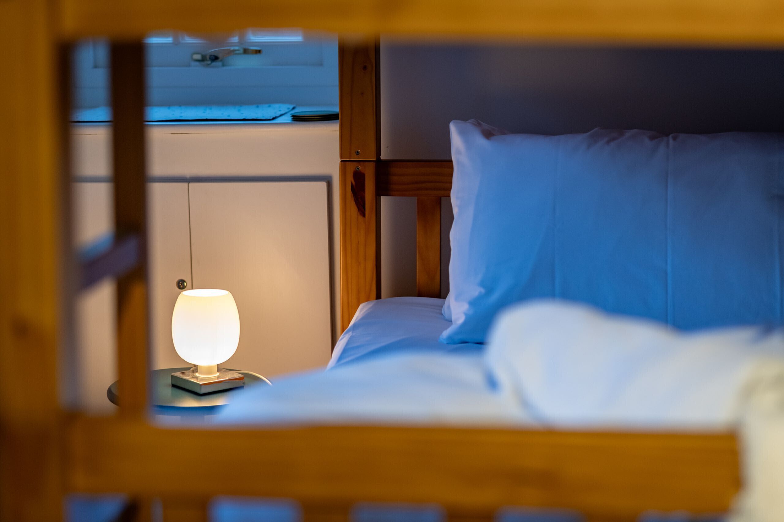A bed with white bedding and a blue pillow, a bedside table with a lamp, and a wooden headboard.