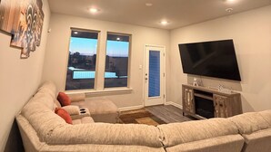 Uma sala de estar com sofá seccional, televisão de tela plana e uma janela grande com vista para um corpo d'água.