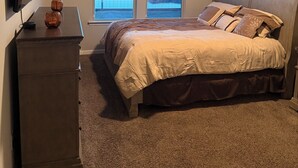 Quarto com cama, penteadeira e televisão. Há duas janelas com vista para uma ponte e paisagem.