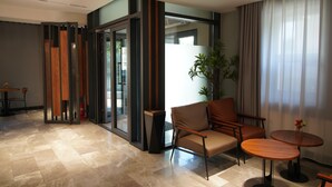 A modern hotel room with a large sliding glass door, a seating area with a sofa and two small round tables, and a potted plant. - Happiness Hotel (Ulaanbaatar)