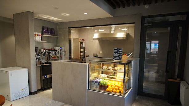 A modern kitchen area with a refrigerator, coffee machine, and a glass display case with oranges. - Happiness Hotel (Ulaanbaatar)
