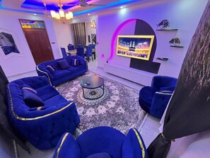 Una sala de estar moderna con sofás azules, una mesa de centro y un televisor montado en la pared.