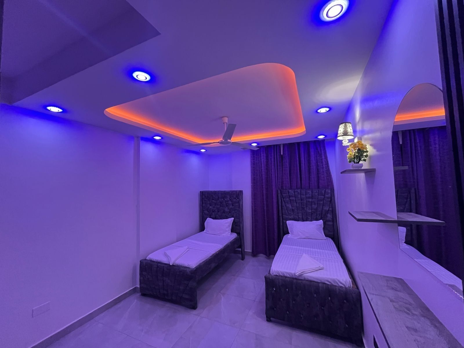 A modern bedroom with two beds, a ceiling fan, and ambient lighting.