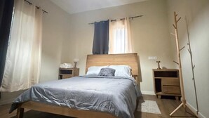Un dormitorio con una cama de madera, una mesita de noche, una lámpara de pie y una ventana con cortinas.