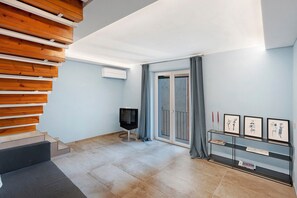 A modern living room with a wooden staircase, a flat-screen TV, a glass door leading outside, and a wall-mounted shelf with framed artwork. - Holiday Home 'Civico 32' with Sea View, Wi-Fi and Air Conditioning (Salerno)