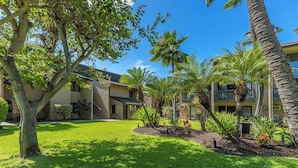 A courtyard with a lawn, palm trees, and a building with multiple balconies. - Ocean view loft with pool and hot tub near Kihei beaches summer deals (Kihei)