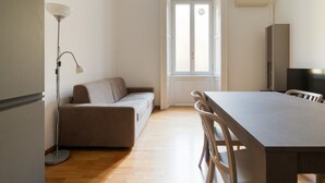 Une pièce comprenant un canapé, une table à manger avec des chaises, un lampadaire et une fenêtre.