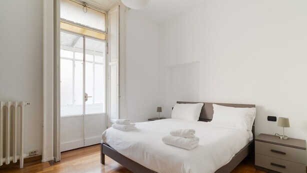 Une chambre à coucher avec un lit, des tables de chevet, un radiateur et une fenêtre.