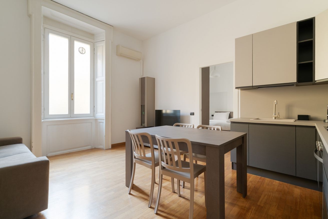 A modern kitchen with a dining table and chairs, a built-in oven, and a window with a view.